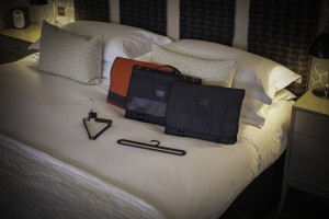 The compact and versatile range of Protégé folding garment bags on a hotel bed